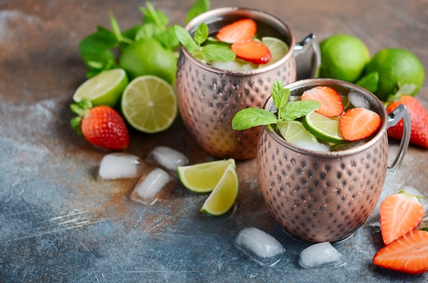 Cóctel de mula de Moscú con cerveza de jengibre, vodka, lima, fresas y menta en tazas de cobre