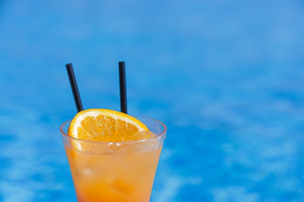Cóctel de naranja con dos pajitas en un fondo de piscina azul closeup copyspace Foto de alta calidad