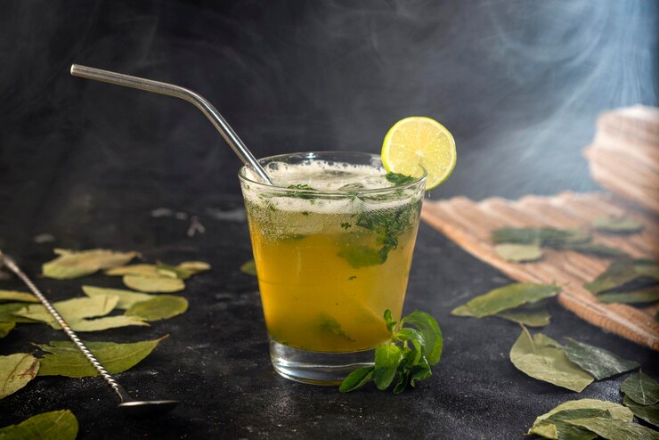 Cóctel o bebida con hojas y limón y vaso de vidrio y humos.