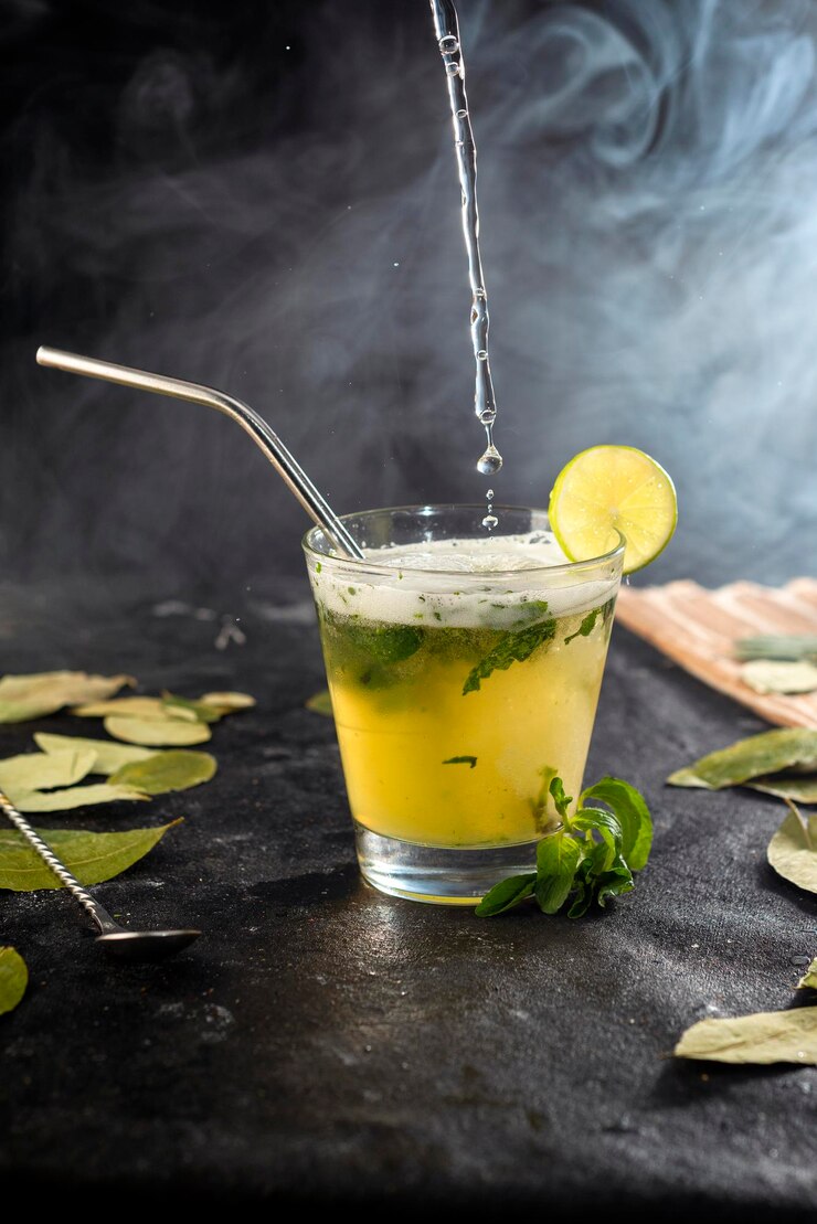 Cóctel o bebida vertiendo en vaso de vidrio con hojas y limón y humos
