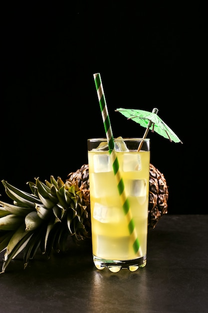 Cóctel de piña con tubo de hielo y paraguas sobre una fruta tropical negra, humor de verano en un estilo oscuro.