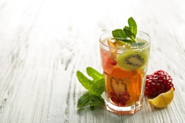 Cóctel refrescante con semillas de granada de menta helada y rodajas de frutas sobre fondo de madera clara