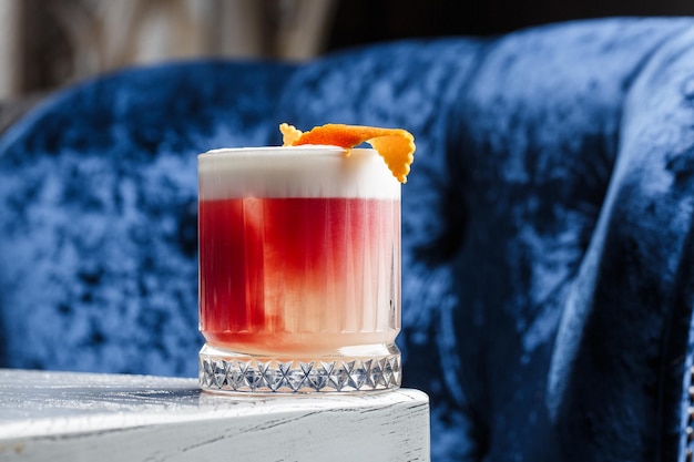 Cóctel rojo clásico a la antigua en un vaso retro con hielo y cáscara de naranja en una vista superior de fondo azul
