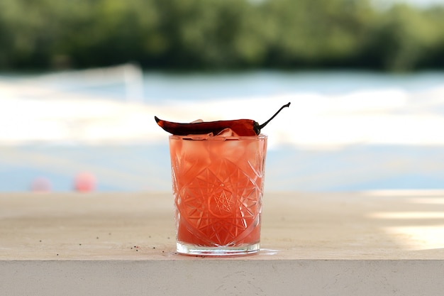 Cóctel rojo con hielo en un vaso de precipitados con pimiento rojo picante