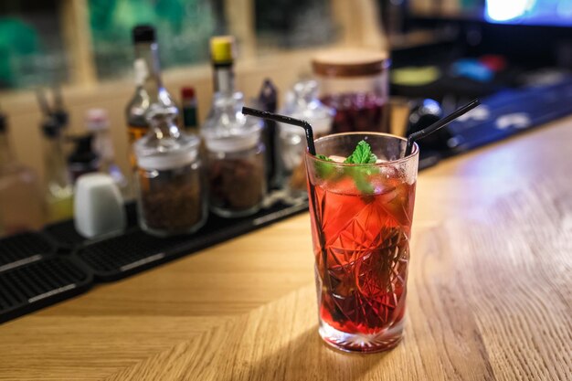 Cóctel rojo en un vaso con menta y dos tubos sobre una mesa en un bar de lujo