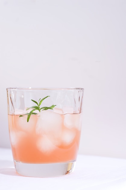 Cóctel rosa con romero y hielo en vaso sobre un mantel blanco sobre la mesa