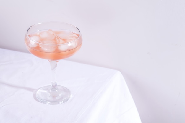 Cóctel rosa con romero y hielo en vaso sobre un mantel blanco sobre la mesa