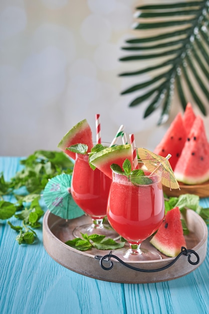 Cóctel de sandía con menta y hielo. Bebidas refrescantes de verano en vasos sobre una mesa de madera azul. Concepto de alimentación saludable en verano.