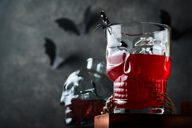 Cóctel sangriento de Halloween Copa de cristal de cóctel rojo sangriento para Halloween y calavera en forma de botella sobre fondos oscuros Fiesta de Halloween con ojos de caramelo murciélagos arañas Dia de los muertos Clousup