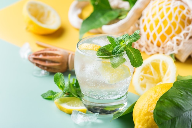 Cóctel de seltzer duro con limón, menta y hielo sobre una mesa. Bebida refrescante de verano, bebida con accesorios de moda sin desperdicio, paja de bambú y bolsa de malla.