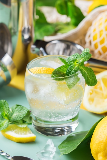 Cóctel de seltzer duro con limón, menta y hielo sobre una mesa. Bebida refrescante de verano, bebida con accesorios de moda sin desperdicio, paja de bambú y bolsa de malla.