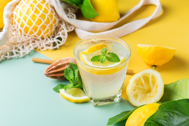 Cóctel de seltzer duro con limón, menta y hielo sobre una mesa. Bebida refrescante de verano, bebida con accesorios de moda sin desperdicio, paja de bambú y bolsa de malla.