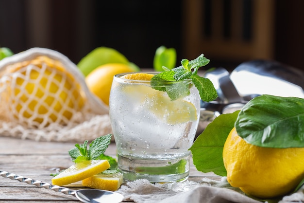 Cóctel de seltzer duro con limón, menta y hielo sobre una mesa. Bebida refrescante de verano, bebida con accesorios de moda sin desperdicio, paja de bambú y bolsa de malla.