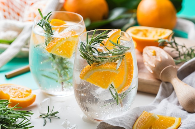 Cóctel de seltzer duro con naranja, romero y hielo sobre una mesa. Bebida refrescante de verano, bebida con accesorios de moda sin desperdicio, paja de bambú y bolsa de malla.