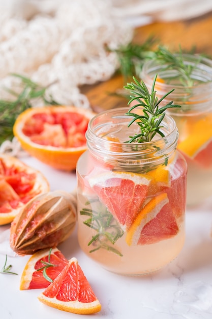 Cóctel de seltzer duro con pomelo, romero y hielo sobre una mesa. Bebida refrescante de verano, bebida en una mesa blanca