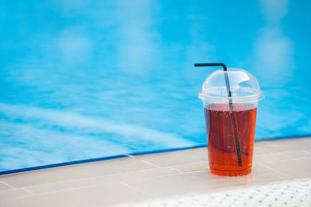 Cóctel tropical de hielo en un vaso de plástico para llevar en el bar de la piscina en el fondo del complejo
