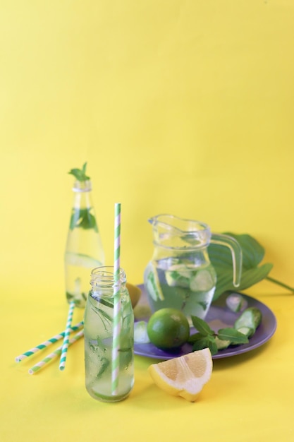 Cóctel útil de rodajas de limón limas hojas de menta en botellas de vidrio sobre un fondo amarillo