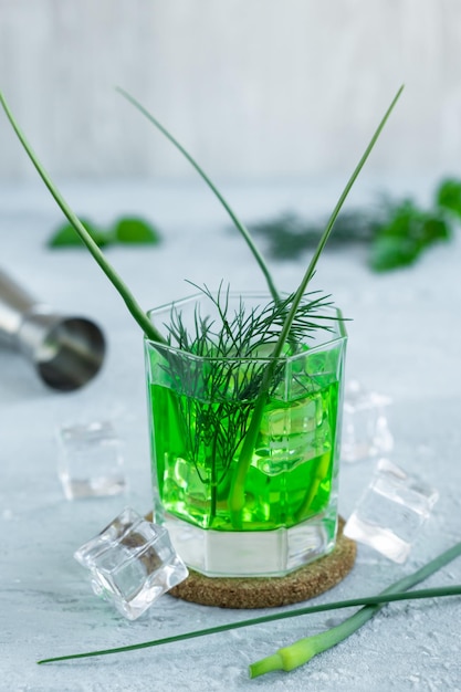 Foto cóctel verde fresco y saludable con flecha de hinojo y ajo en vidrio con cubitos de hielo en una mesa de concreto