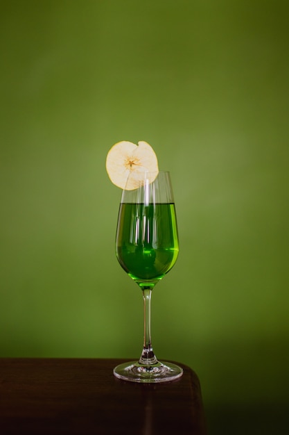 Un cóctel verde en un vaso de flauta adornado con una rodaja de manzana deshidratada