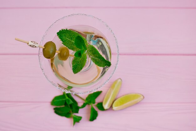 Cóctel de vermut en una copa alta de martini con aceitunas y menta sobre un fondo rosa