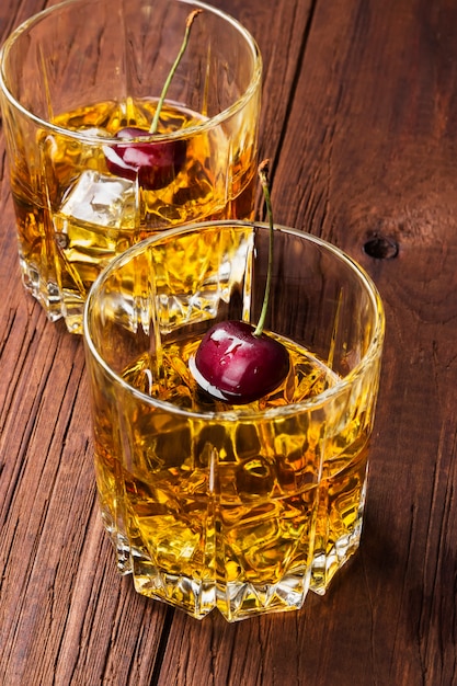 Cóctel de whisky con cereza en dos vasos sobre un fondo de madera