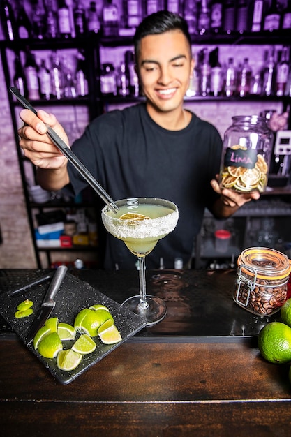 Coctelera frente a un pub bar dejando una rodaja de limón en un cóctel