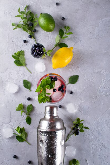 Coctelera, limón, lima, hojas de menta, arándanos y hielo para preparar un cóctel de verano.