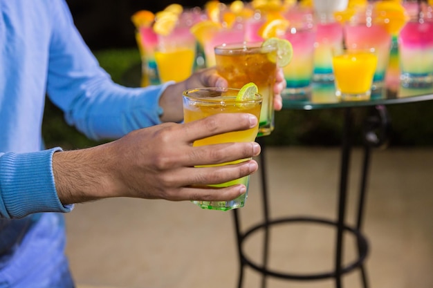 Cócteles de alcohol de diferentes colores con rodajas de naranja en una fiesta nocturna al aire libre en un hotel de Egipto El hombre sostiene vasos Mesa de catering decorada en un evento al aire libre