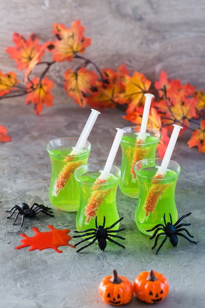 Cócteles de Halloween. Jeringas con sangre en vasos con limonada verde y arañas sobre la mesa.