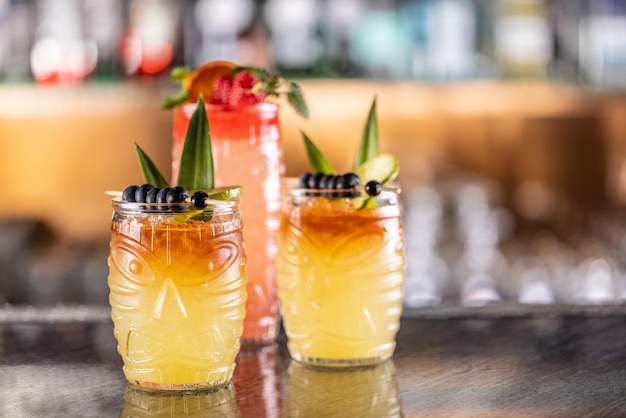 Cócteles mai tai en vasos hawaianos adornados con piña, arándanos y fresas en el mostrador del bar