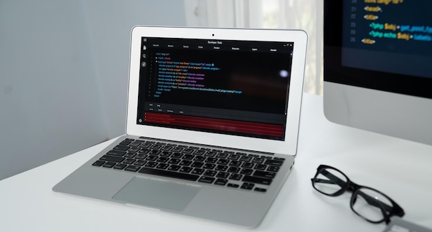 Código de programación en el monitor del portátil y al lado de la pantalla del ordenador de escritorio Tastemaker