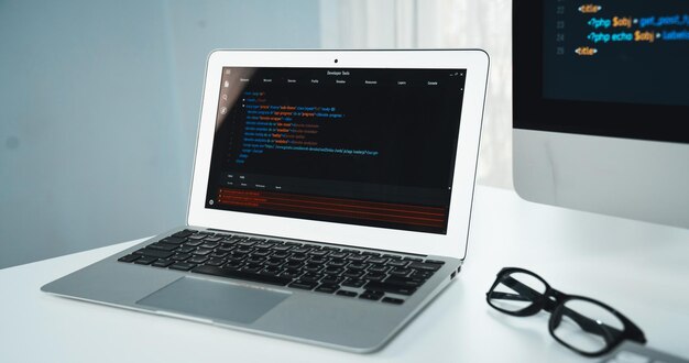 Código de programación en el monitor del portátil y al lado de la pantalla del ordenador de escritorio