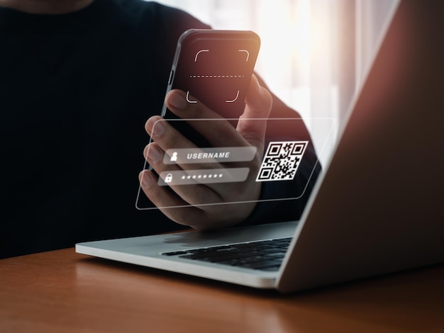 Código QR Concepto de seguridad de autenticación multifactorial Símbolo gráfico del escáner digital en la lente de la cámara del teléfono inteligente sujetada por el hombre de negocios escaneando a mano para iniciar sesión en la pantalla virtual desde la computadora portátil