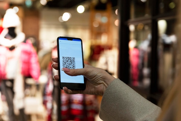 Código QR em um smartphone na mão de uma mulher em uma loja de roupas em um shopping center. Passe verde para estilo de vida durante uma pandemia. Fechar-se.