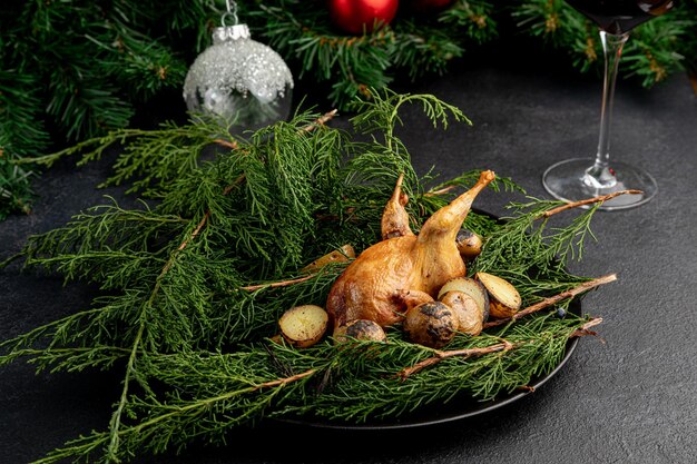 Codorna frita em um prato decorado com galhos verdes com um copo de vinho tinto em um fundo escuro de natal