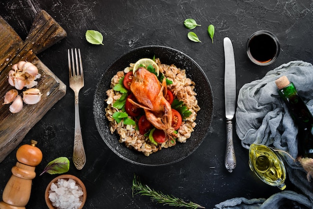 Codornices al horno con avena y verduras. Sobre un fondo negro. Vista superior. Espacio libre para su texto.