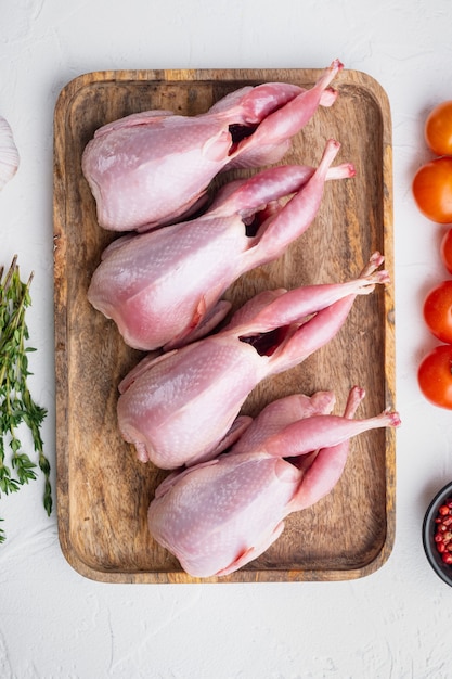 Codornizes de carne crua fresca com ervas, postura plana, sobre fundo branco texturizado