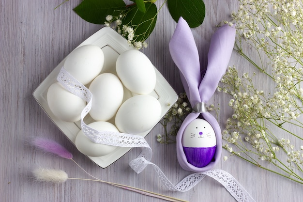 Coelhinho da Páscoa com ovos de Páscoa e flores na mesa de madeira branca