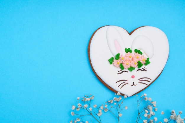 Coelhinho da Páscoa, pão de mel com esmalte e com flores na mesa azul Copie o espaço