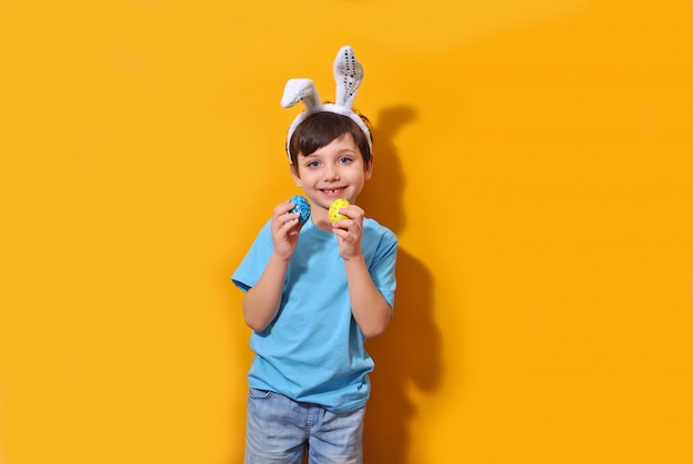 Coelhinho da Páscoa sorridente garoto garoto segurando ovos coloridos sobre o fundo amarelo