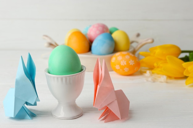 Coelhinhos da Páscoa com ovos coloridos na mesa de madeira contra a luz de fundo