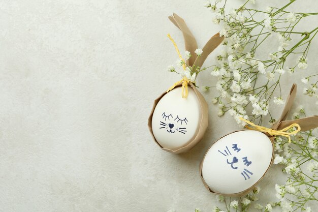 Coelhinhos da Páscoa feitos de ovos e flores de gipsófila em um plano de fundo texturizado branco