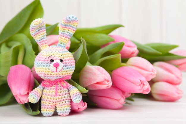 Coelho de malha com delicadas tulipas cor de rosa. Brinquedo de malha, feito à mão, bordado, amigurumi.