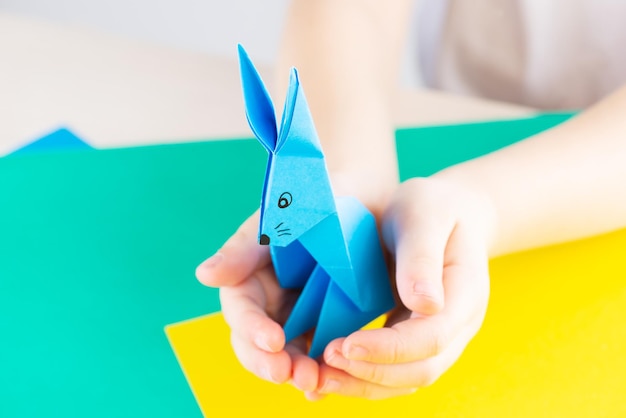 Coelho de papel azul origami em uma mesa nas mãos de uma criança