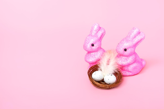 Foto coelhos de páscoa e um ninho com ovos em um fundo rosa conceito de feriado close up espaço de cópia
