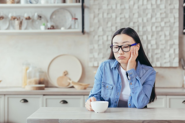 Coffee break jovem asiática cansada freelancer sentada em casa na mesa da cozinha com uma xícara de