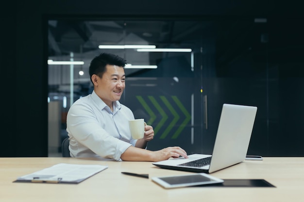 Coffee break um jovem empresário asiático um freelancer bebe café de uma xícara fala de um