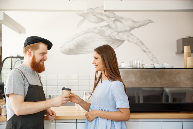 Coffee Business Concept - junge smart bärtigen Barkeeper genießen reden und geben wegnehmen Tasse Kaffee zu hübschen Kunden.