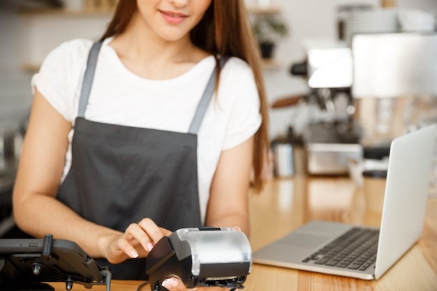 Coffee Business Concept - Schöne weibliche Barista geben Zahlungsdienst für Kunden mit Kreditkarte und lächelnd während der Arbeit an der Bartheke in modernen Café.