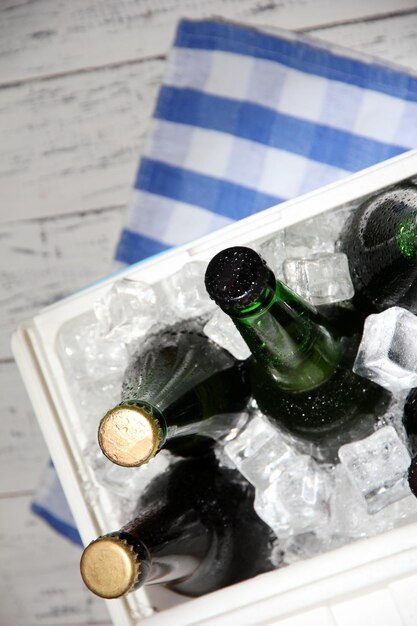 Cofre de hielo lleno de bebidas en botellas en servilleta de color sobre fondo de madera